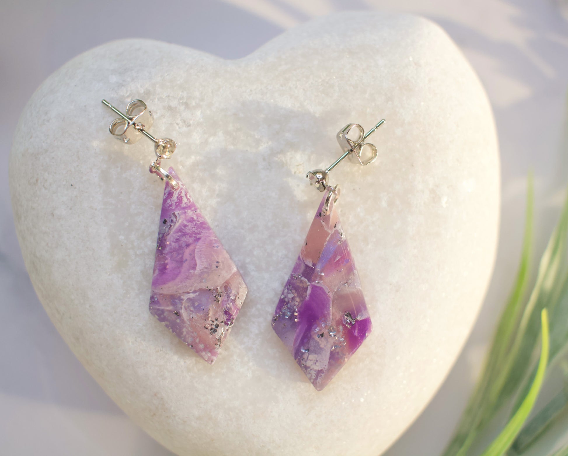 Pair of purple and pink marbled earrings on a white heart-shaped stone.