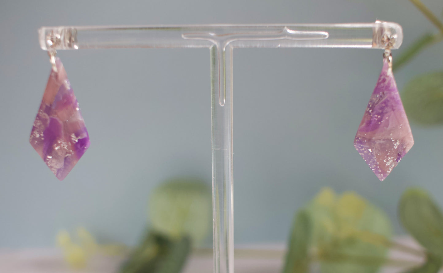 Pink and purple earrings on a clear stand with a blurred green background