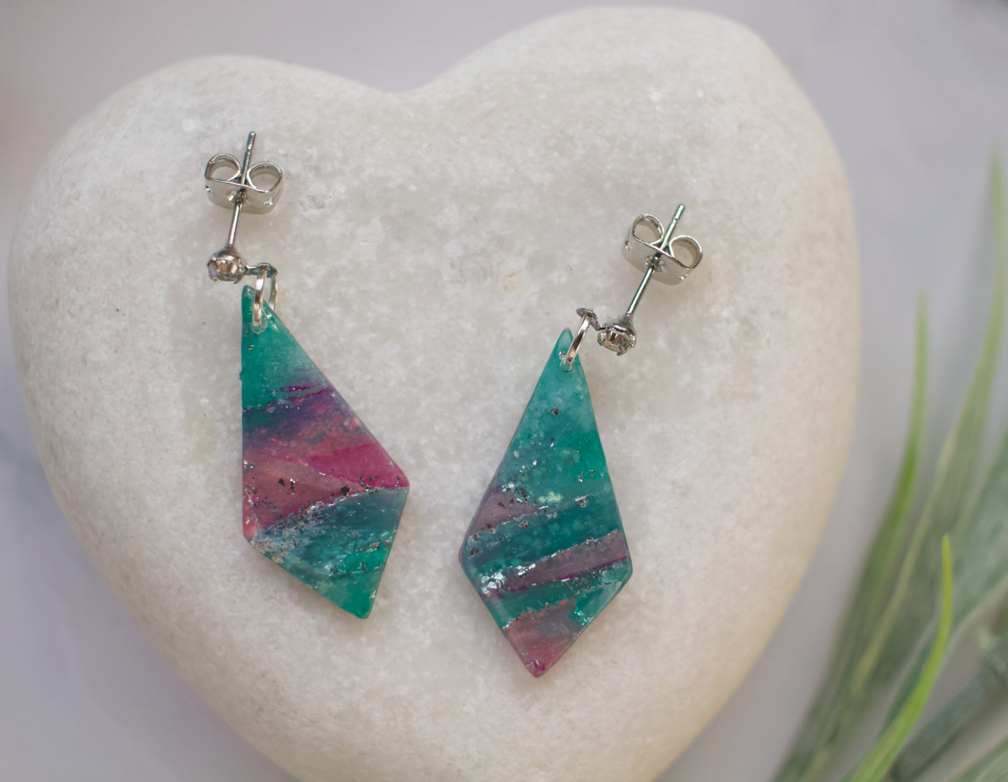 Colorful diamond-shaped earrings on a heart-shaped stone with a blurred natural background