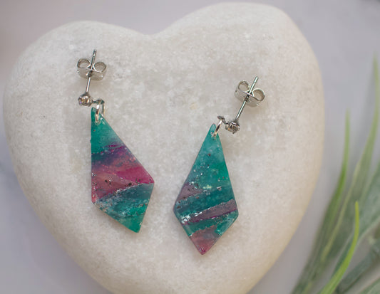 Colorful diamond-shaped earrings on a heart-shaped stone with a blurred natural background