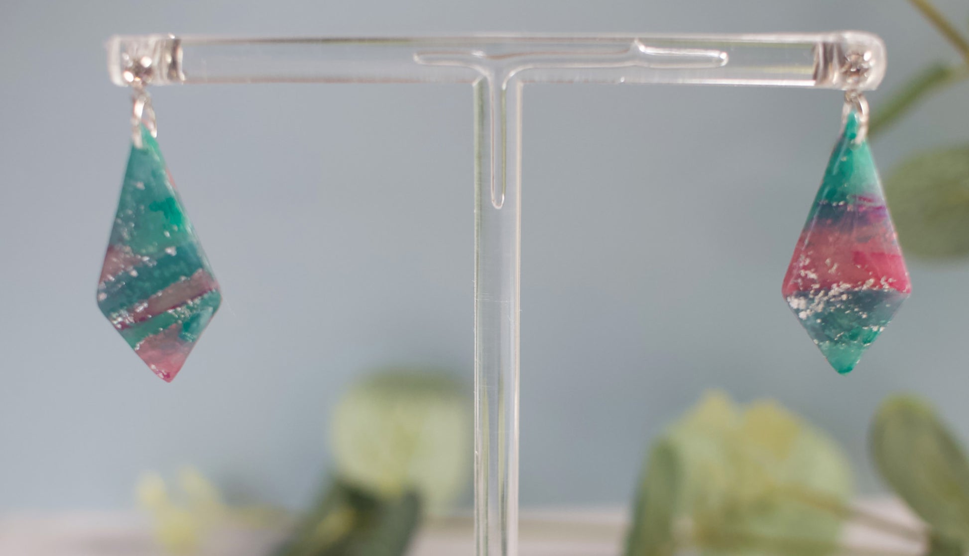 Multicolored teardrop earrings on a clear stand with a blurred green plant background