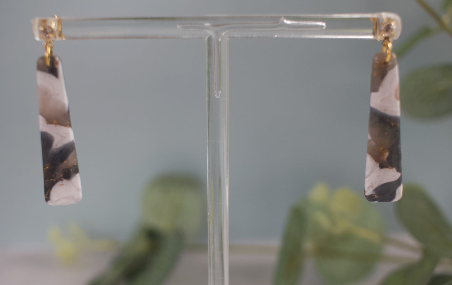 Pair of earrings on a clear stand with a blurred green plant background
