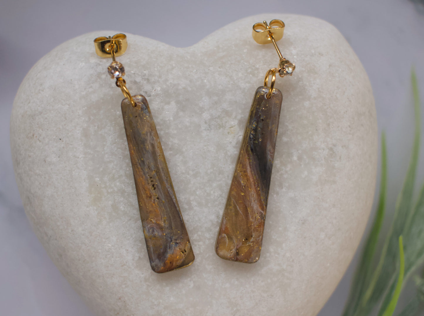 Pair of gold earrings with brown stone drops on a white stone surface.