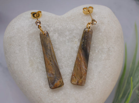 Pair of gold earrings with brown stone drops on a white stone surface.