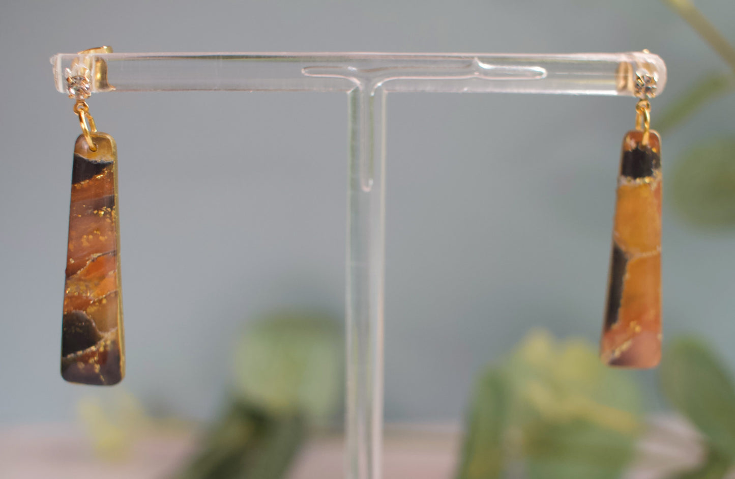 Pair of amber and black marbled earrings on a clear stand with a blurred green background
