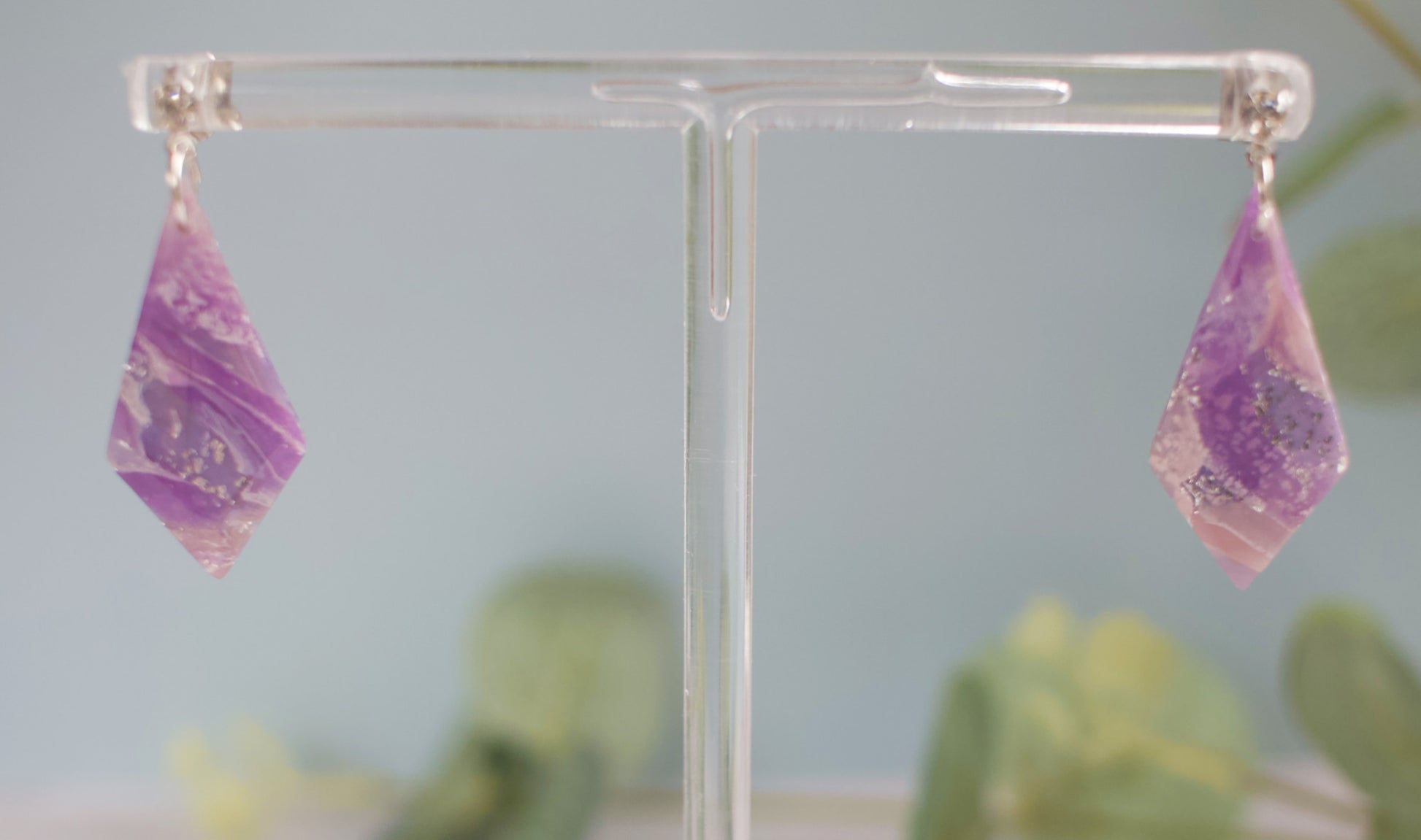 Purple marbled earrings on a clear stand with a blurred green plant background