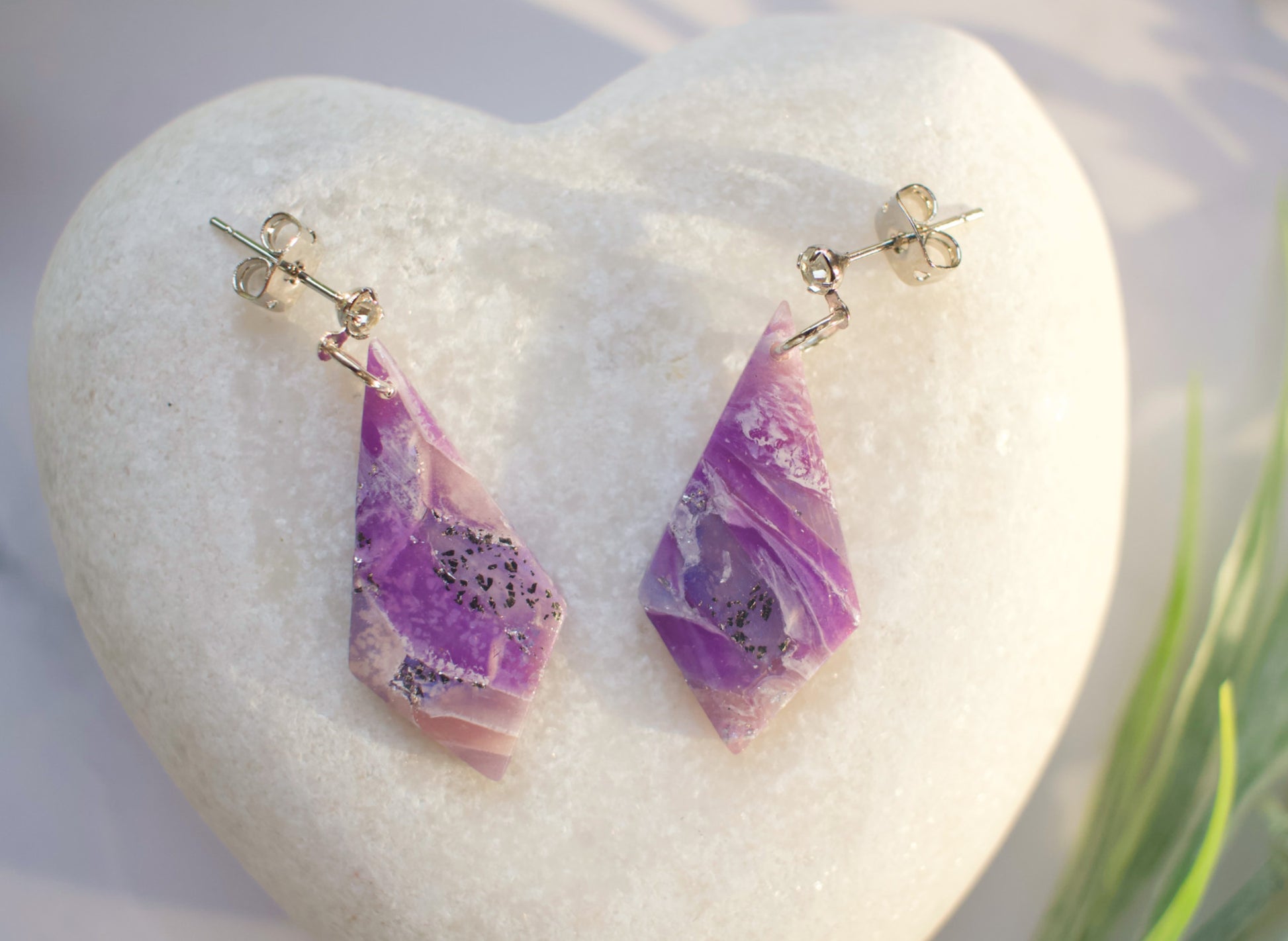 Purple teardrop earrings on a white stone with a natural background
