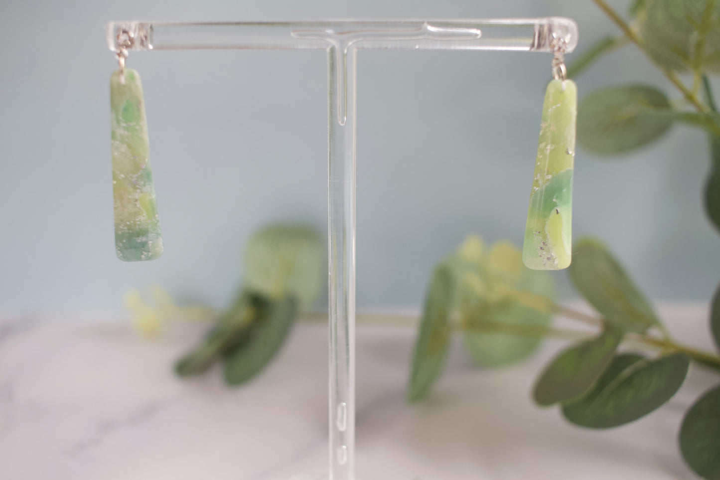 Green earrings on a clear stand with a blurred green leafy background