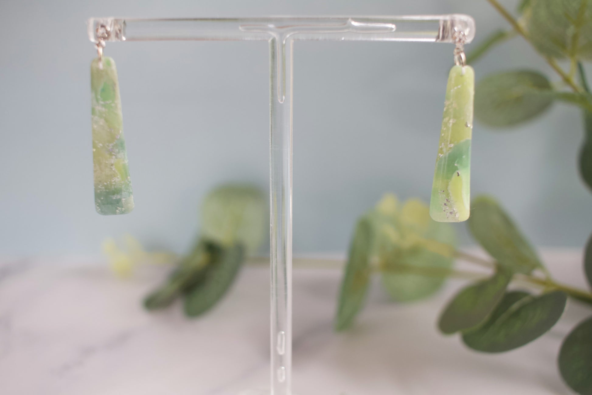 Green earrings on a clear stand with a blurred green leafy background
