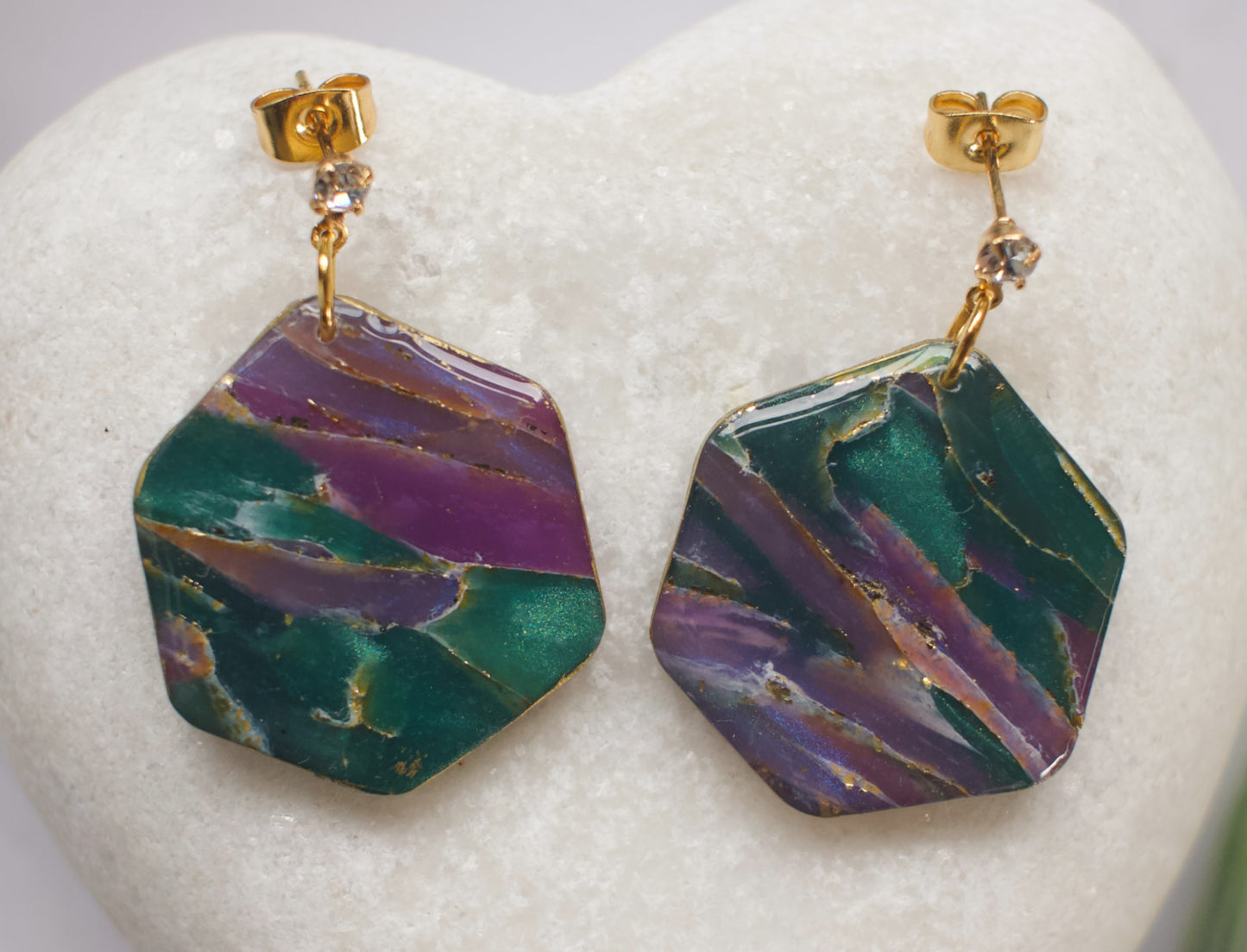 Hexagonal earrings with green and purple marbled stone design on a white heart-shaped stand