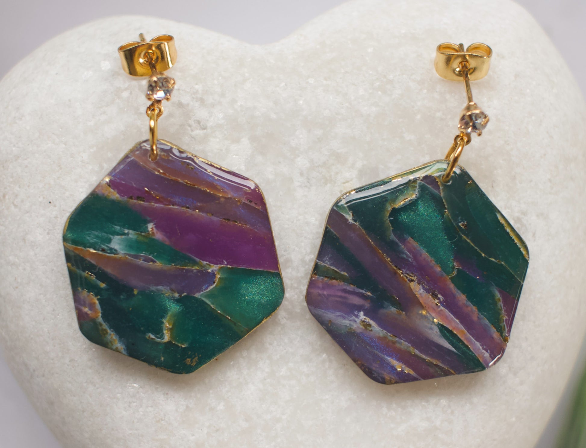 Hexagonal earrings with green and purple marbled stone design on a white heart-shaped stand