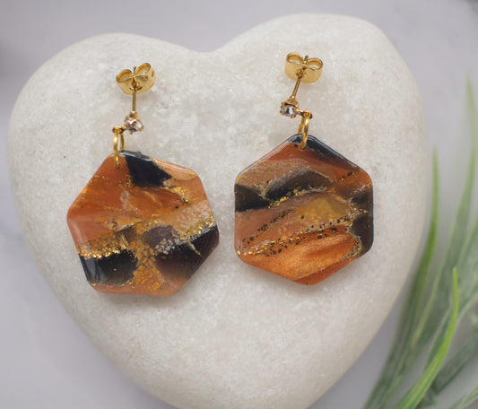 Pair of orange and black marbled hexagon earrings on a heart-shaped stone.