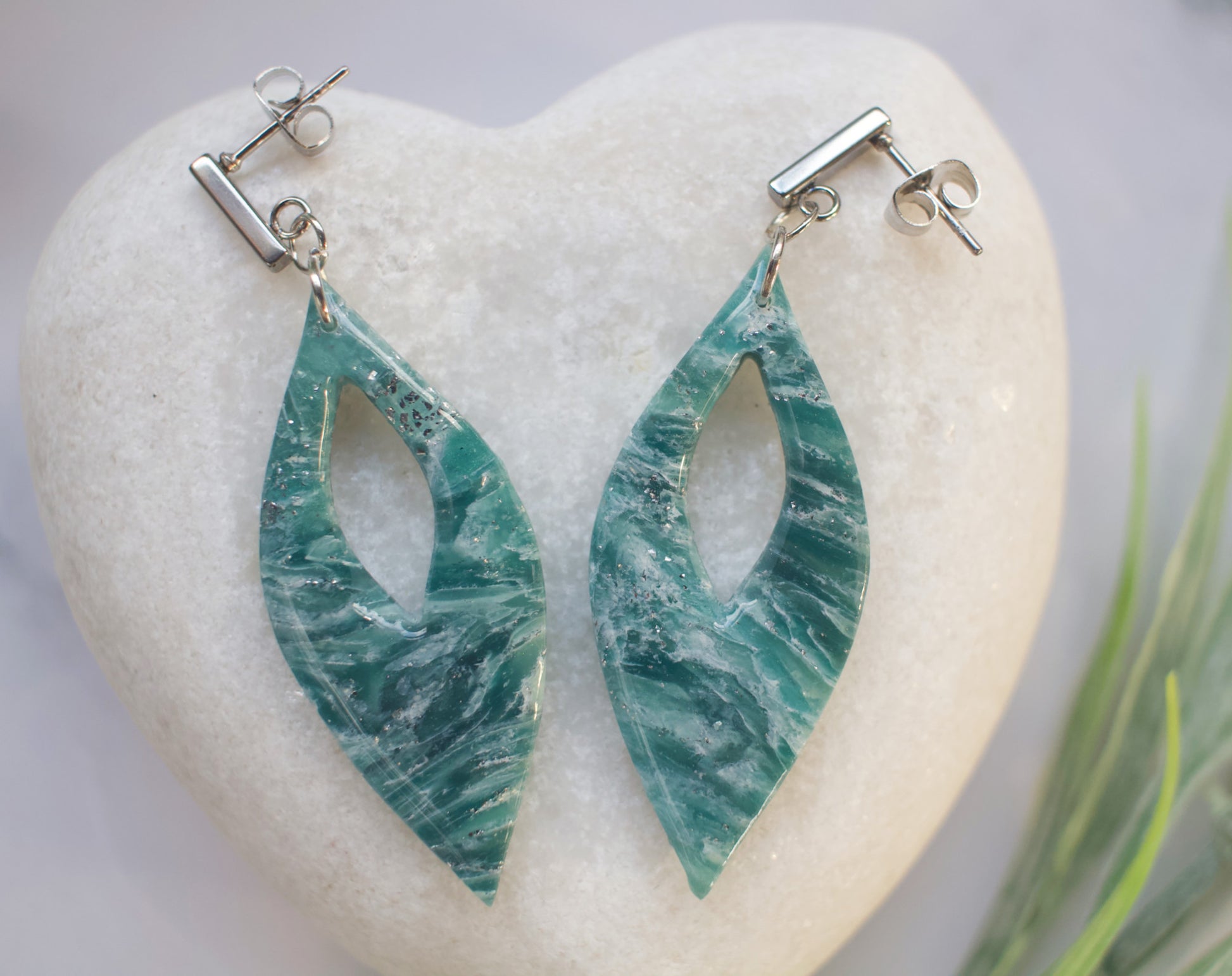 Teal marbled earrings on a white stone with a natural background
