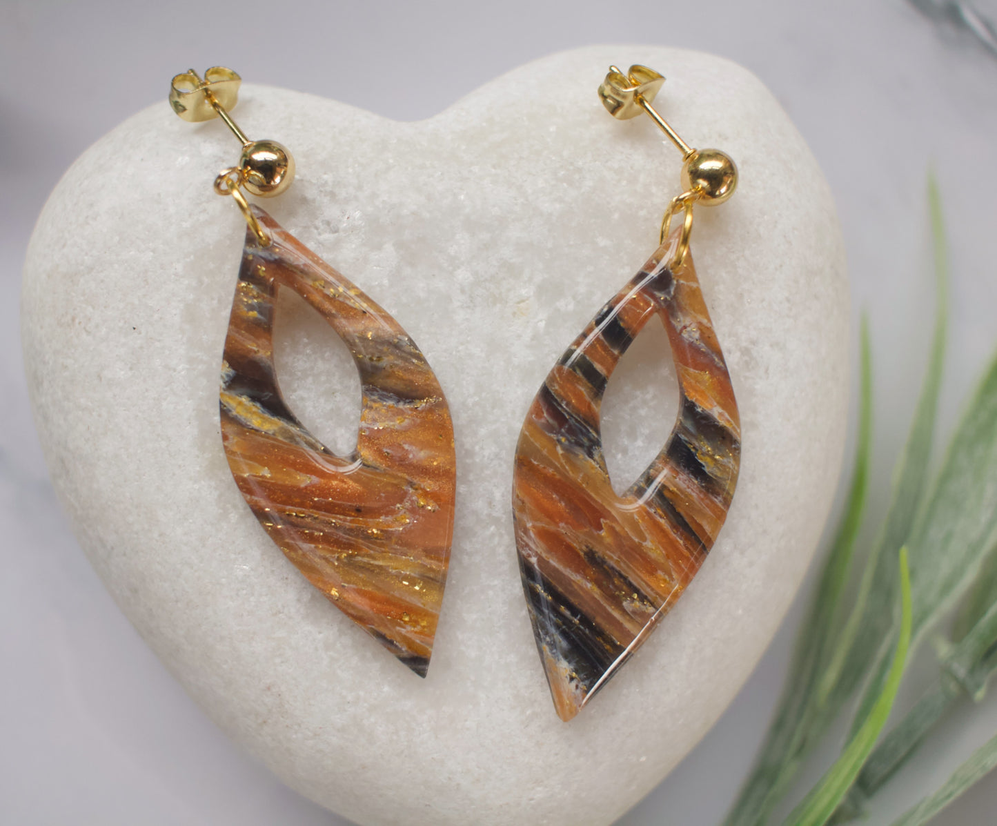 Pair of leaf-shaped earrings with a tiger stripe pattern on a white stone surface.