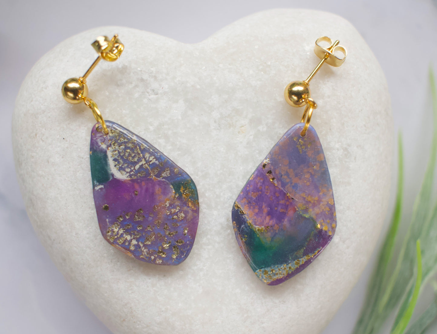 Purple and teal marbled stone effect tear drop earrings displayed on a white heart shaped stone.
