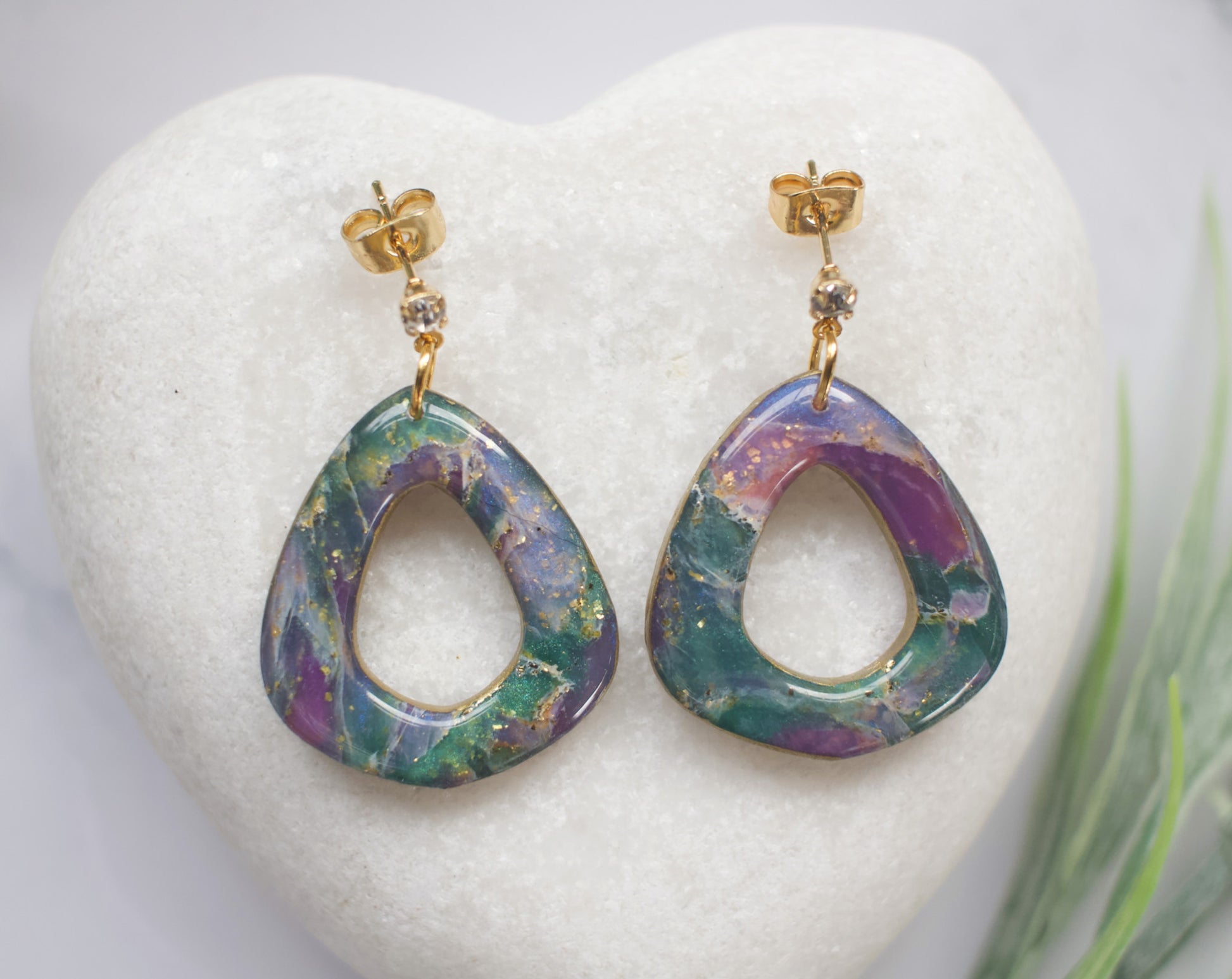 Purple, teal and gold teardrop earrings on a white heart-shaped stand.