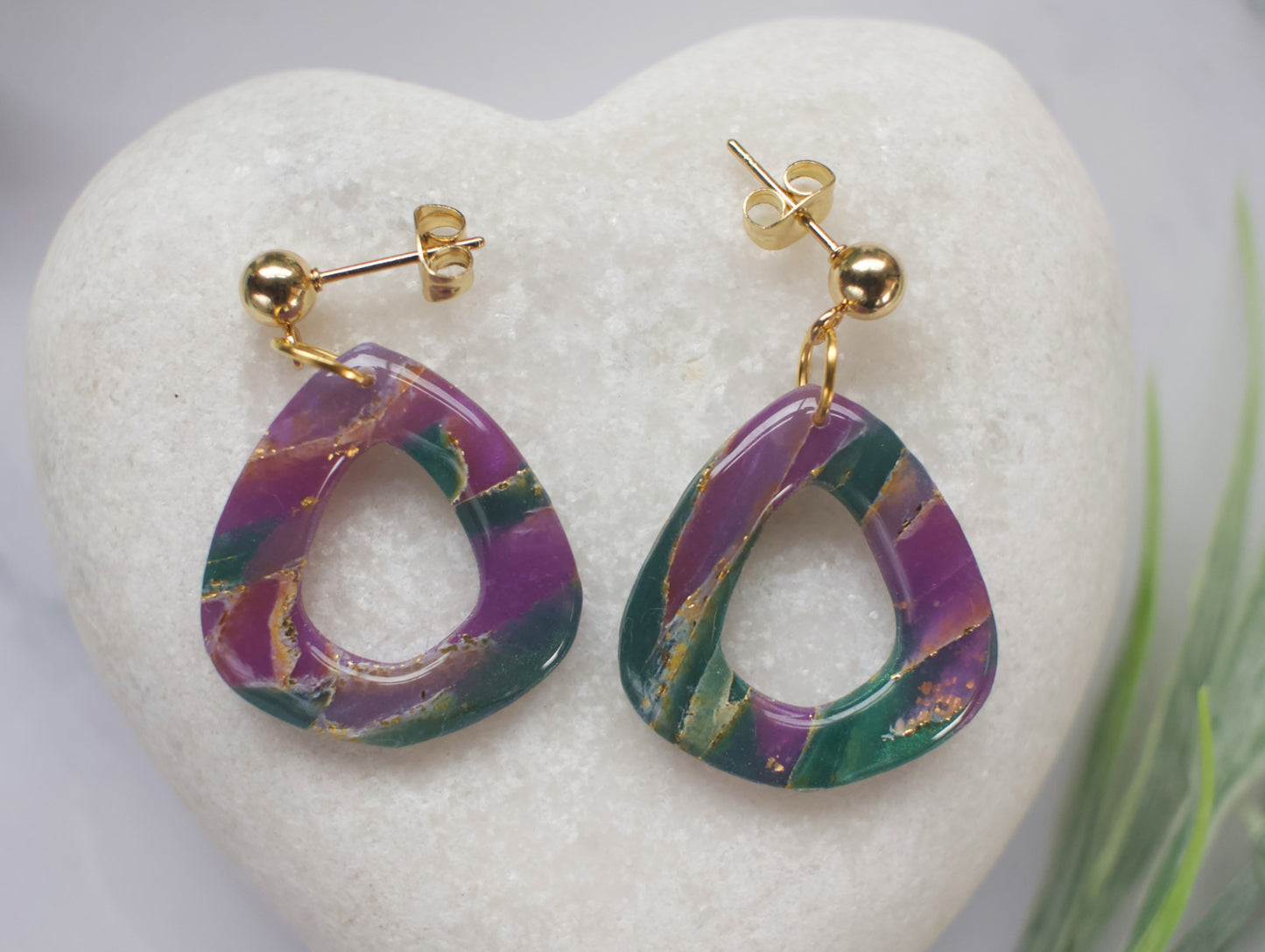 Purple and teal marbled earrings with gold accents on a white heart-shaped stone.