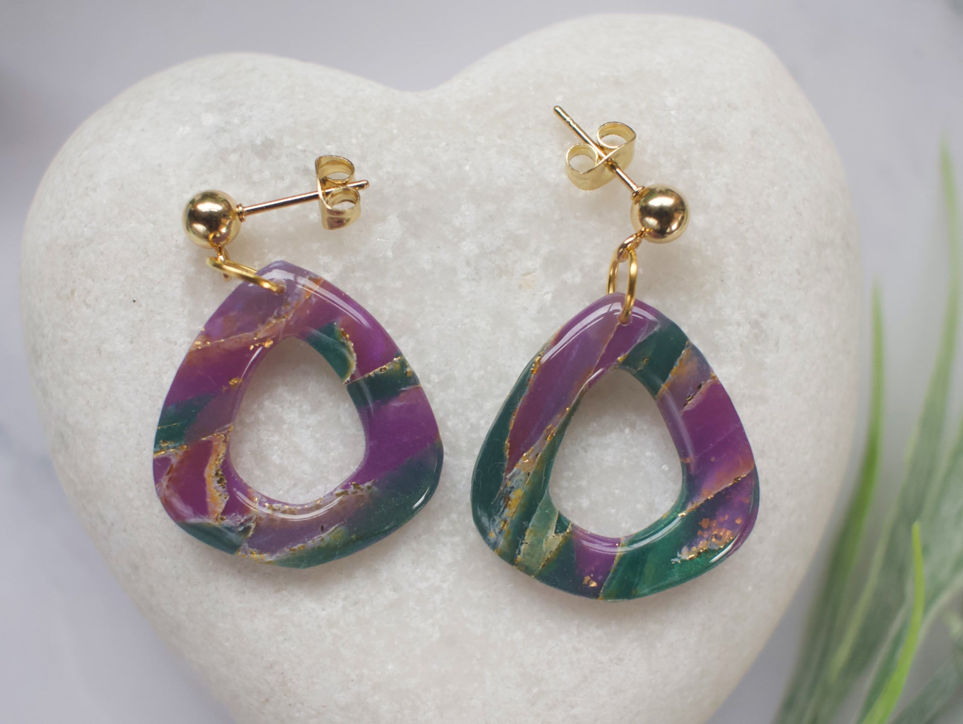 Purple and teal marbled earrings with gold accents on a white heart-shaped stone.