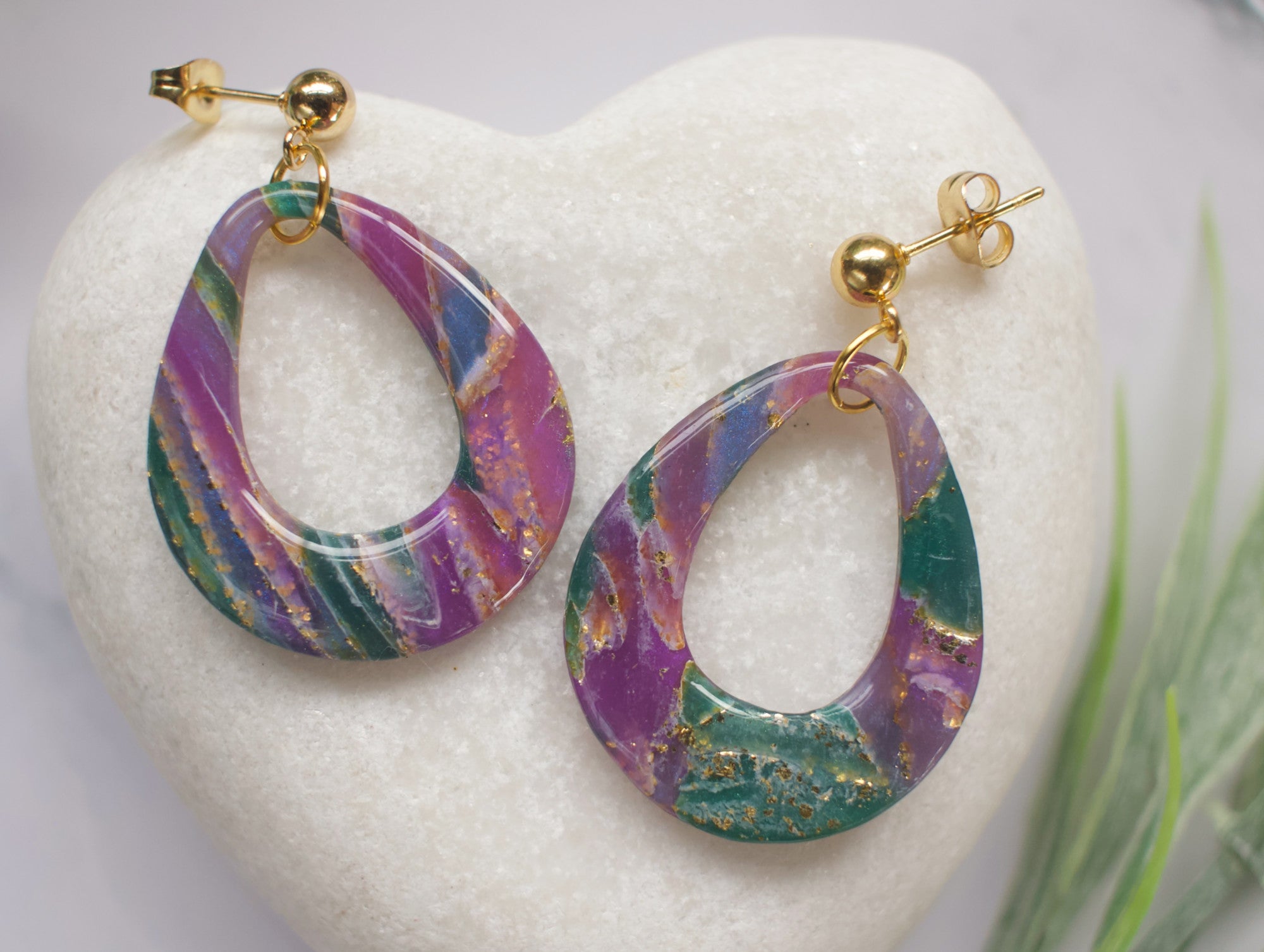 Marbled purple and teal hoop earrings on a white stone surface