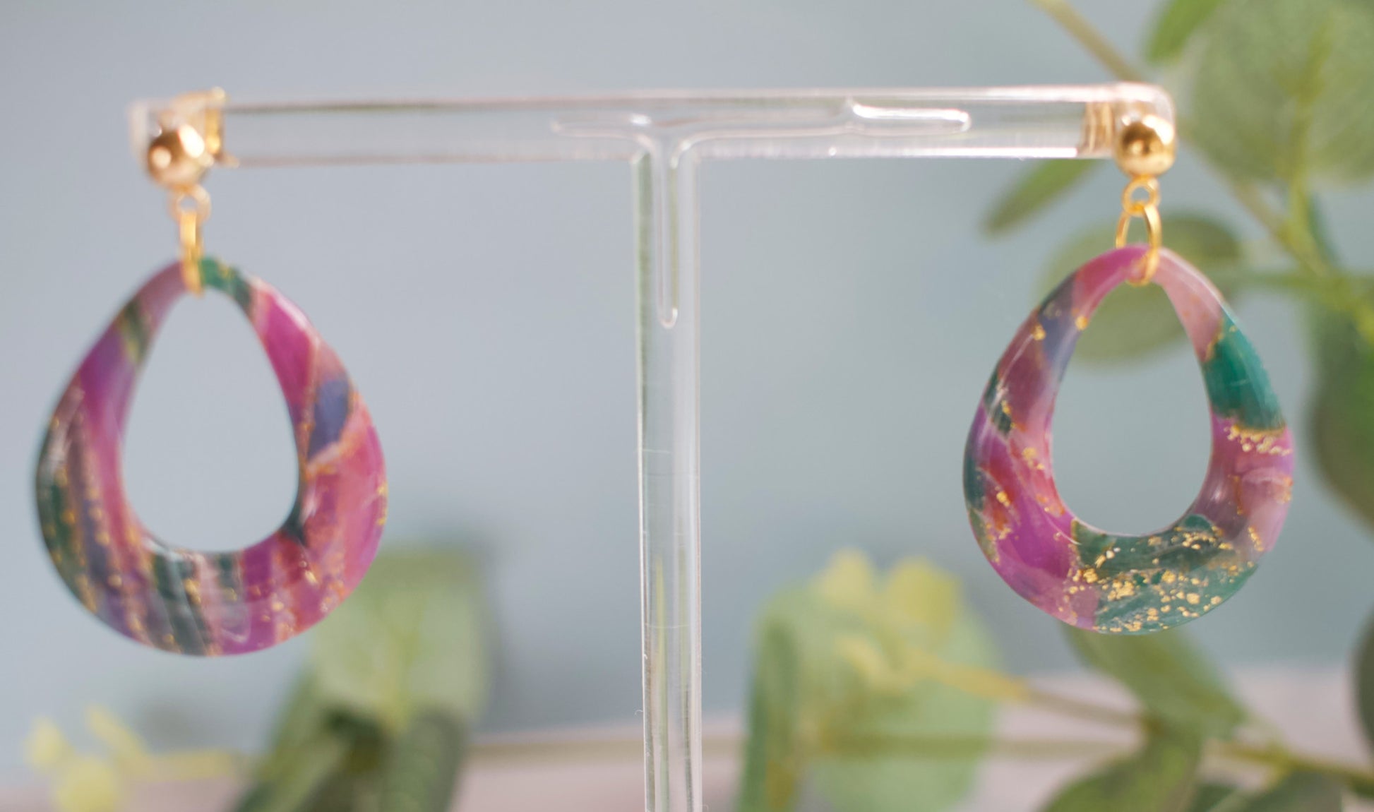 Marbled teal and purple teardrop earrings on a clear stand with a light blue background