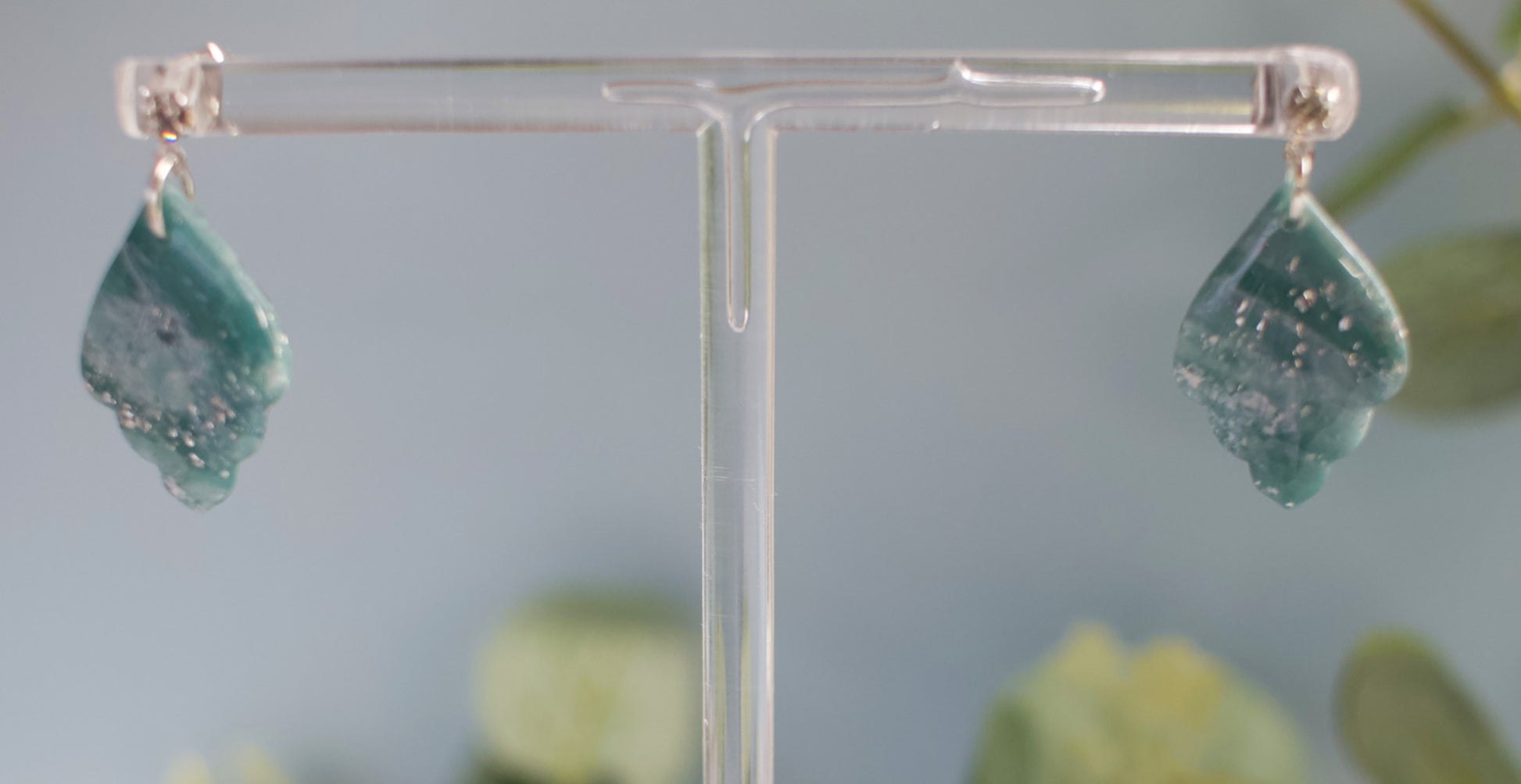 Teal earrings on a clear stand with a blurred green background