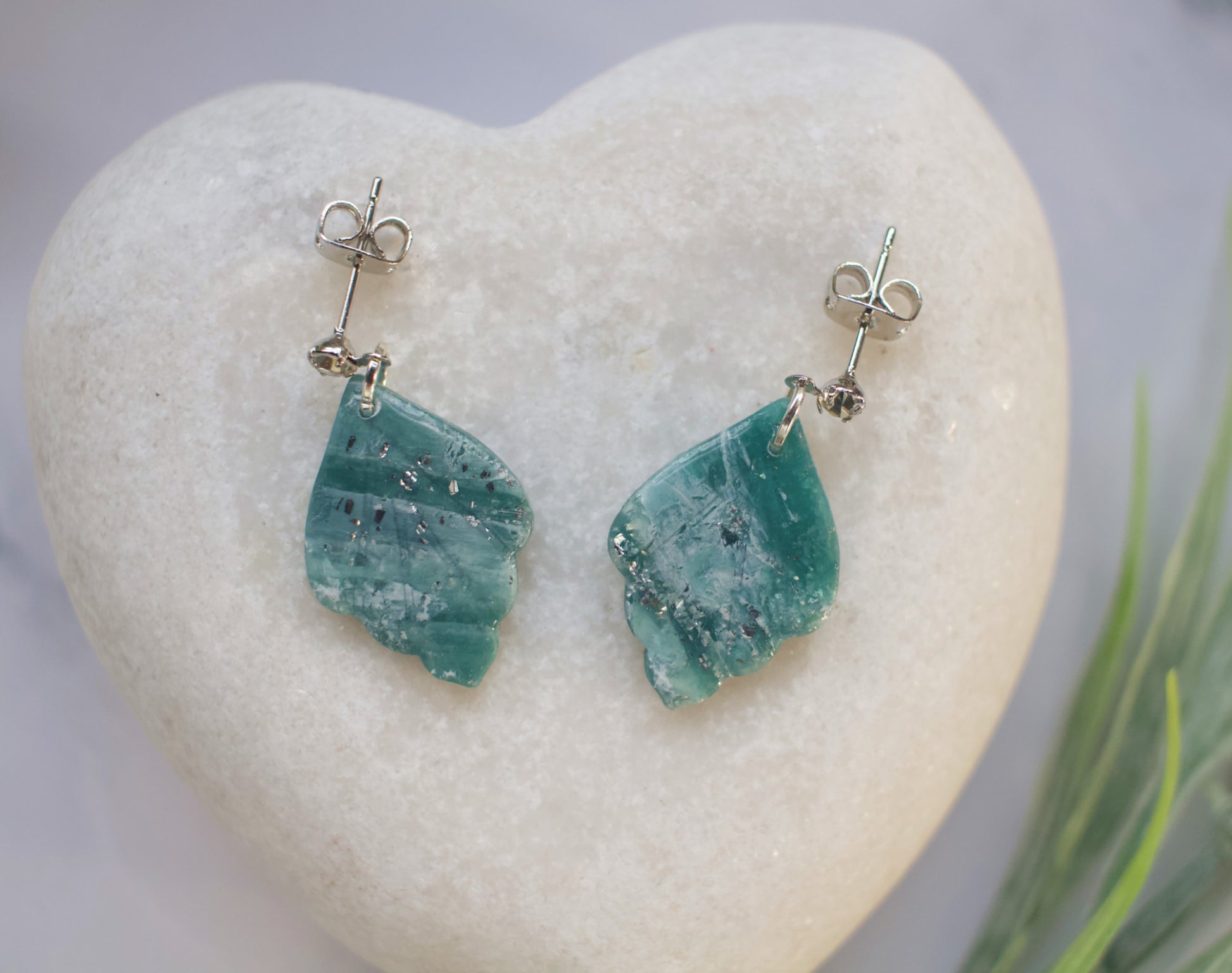 Teal stone earrings on a heart-shaped stone with a blurred natural background