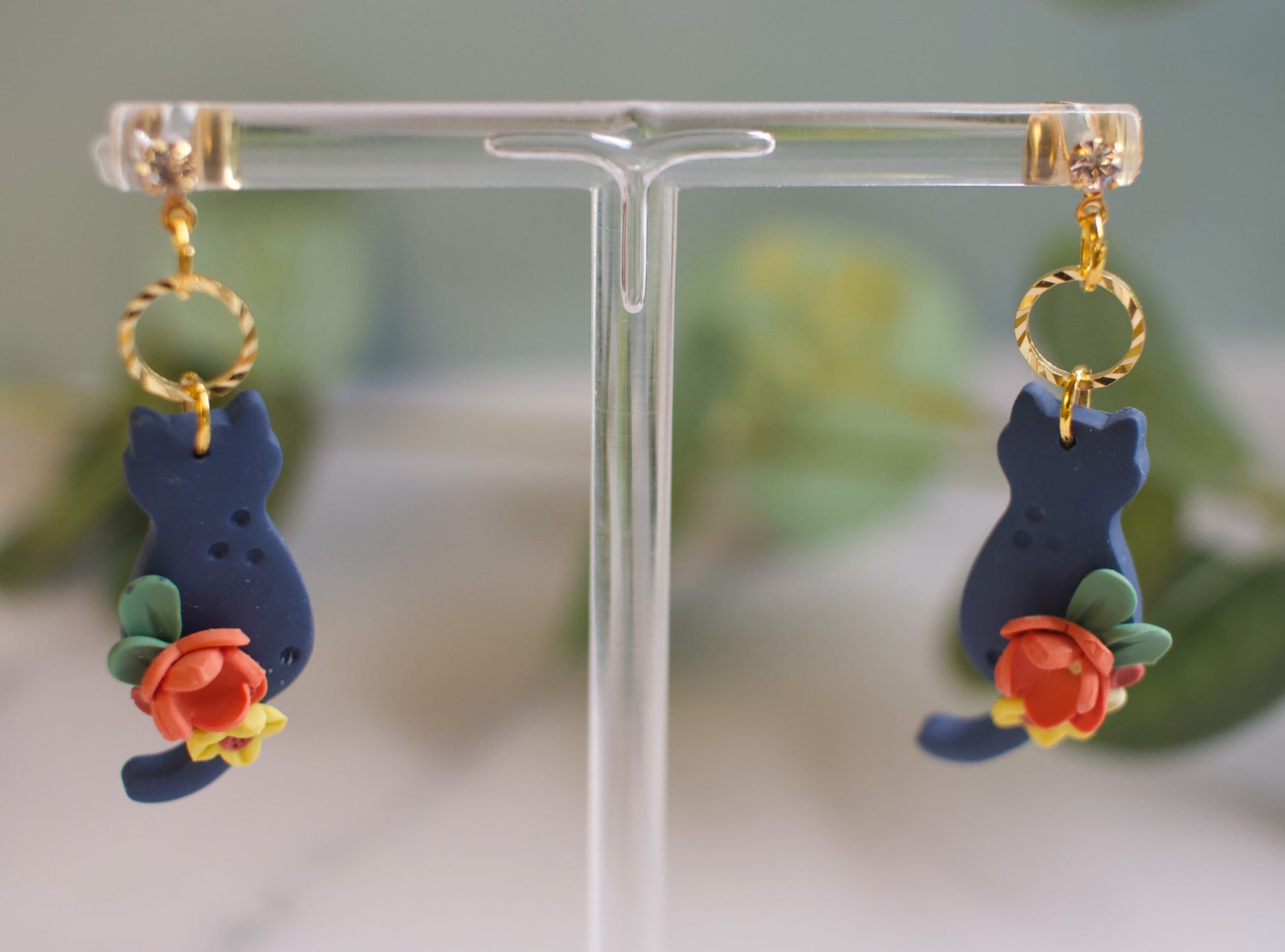 Blue cat-shaped earrings with floral details on a clear stand.