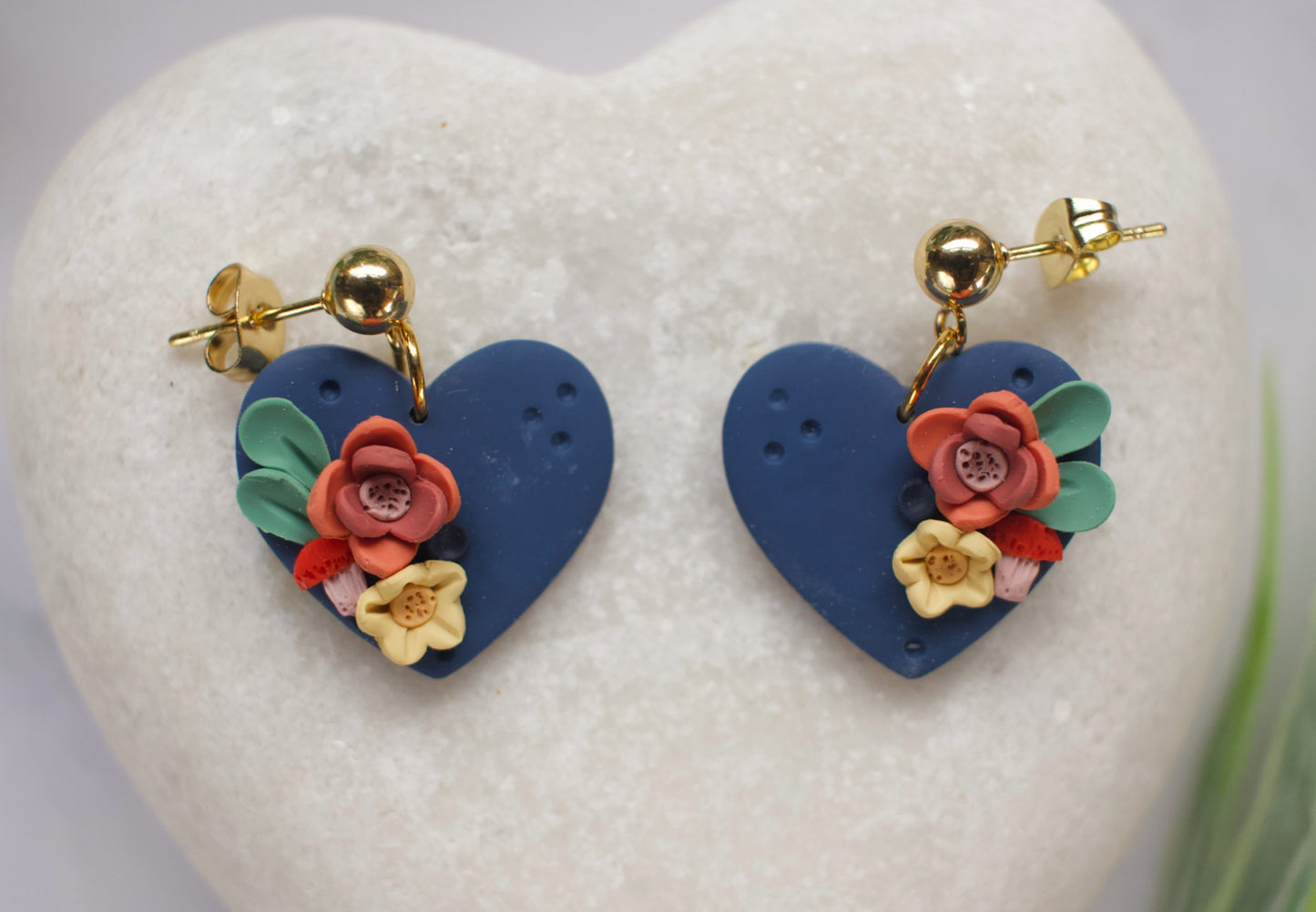 Heart-shaped earrings with floral designs on a heart-shaped stand.