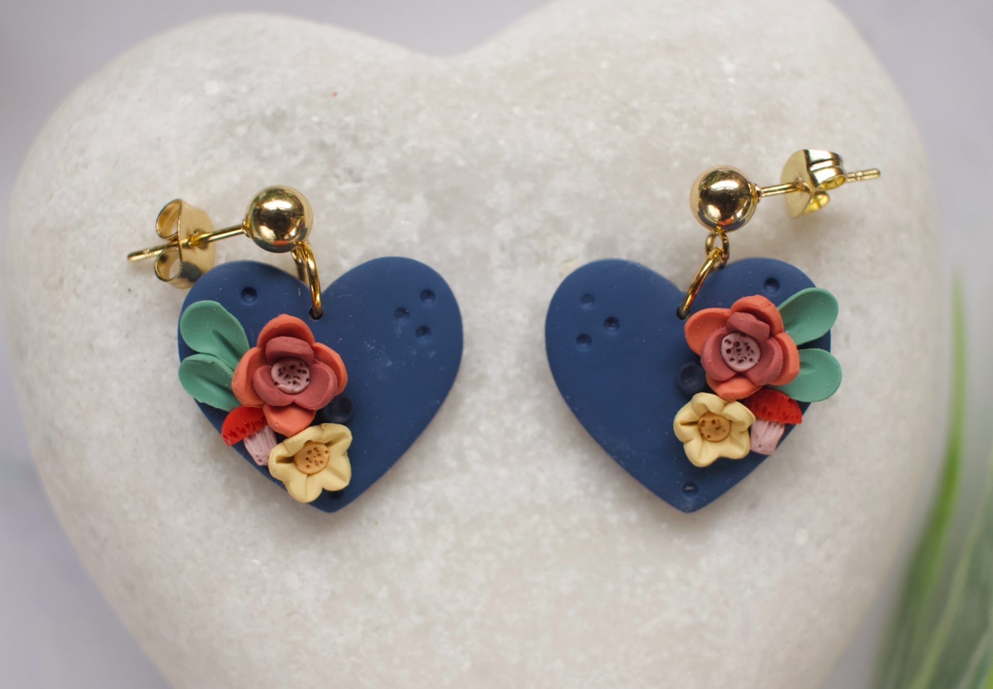Heart-shaped earrings with floral designs on a heart-shaped stand.