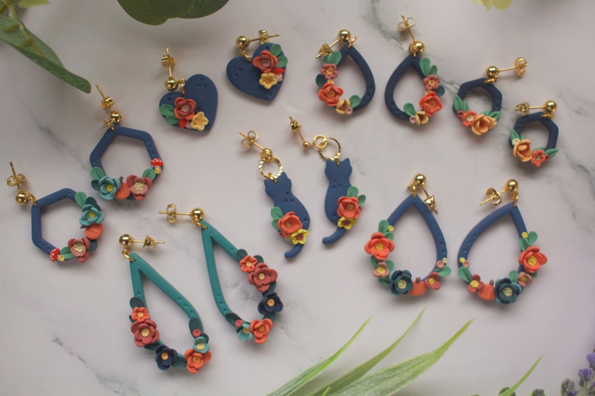 Navy and teal autumnal earring collection with floral designs on a marble surface