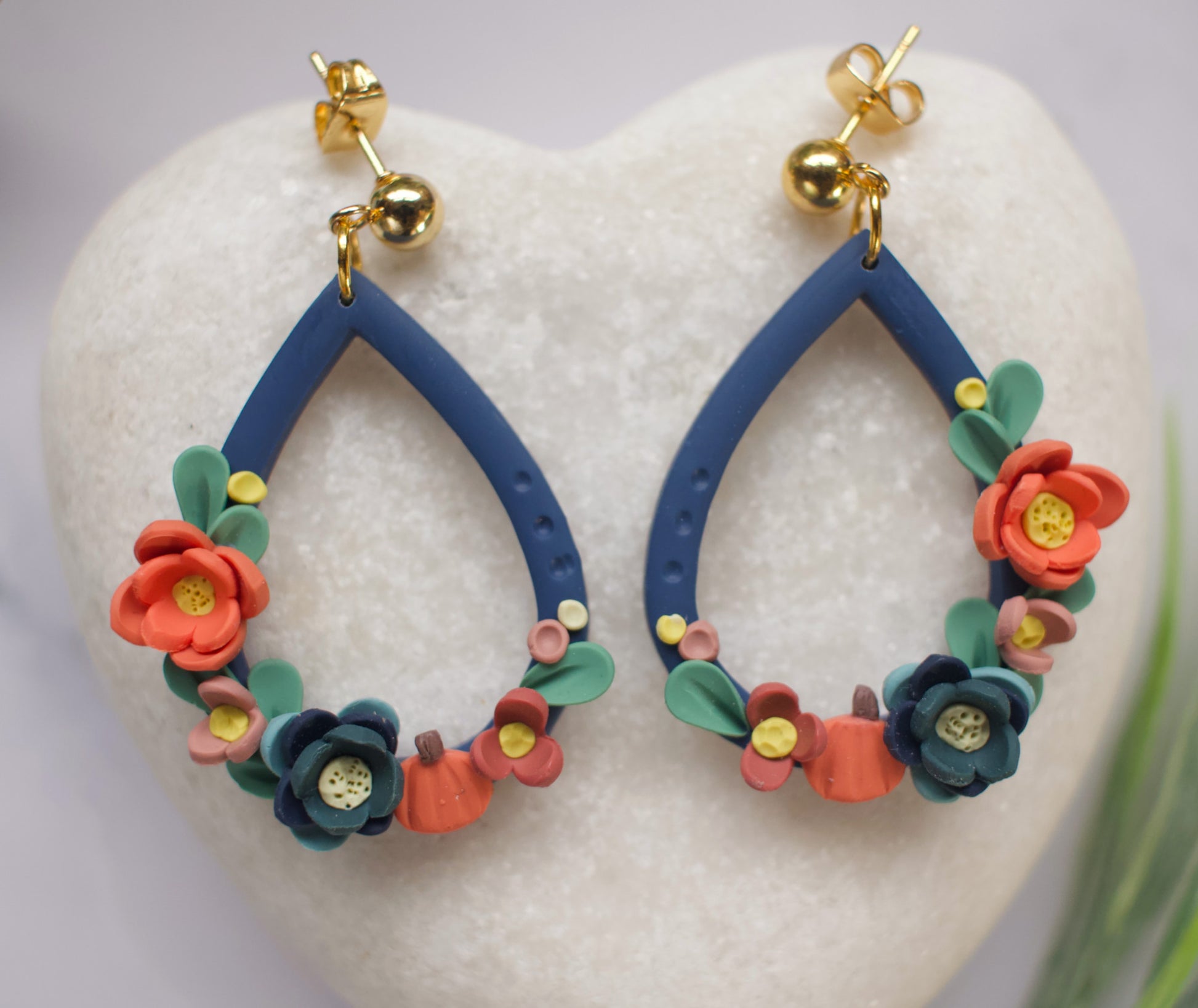 Navy blue teardrop earrings with floral designs on a white heart-shaped stone
