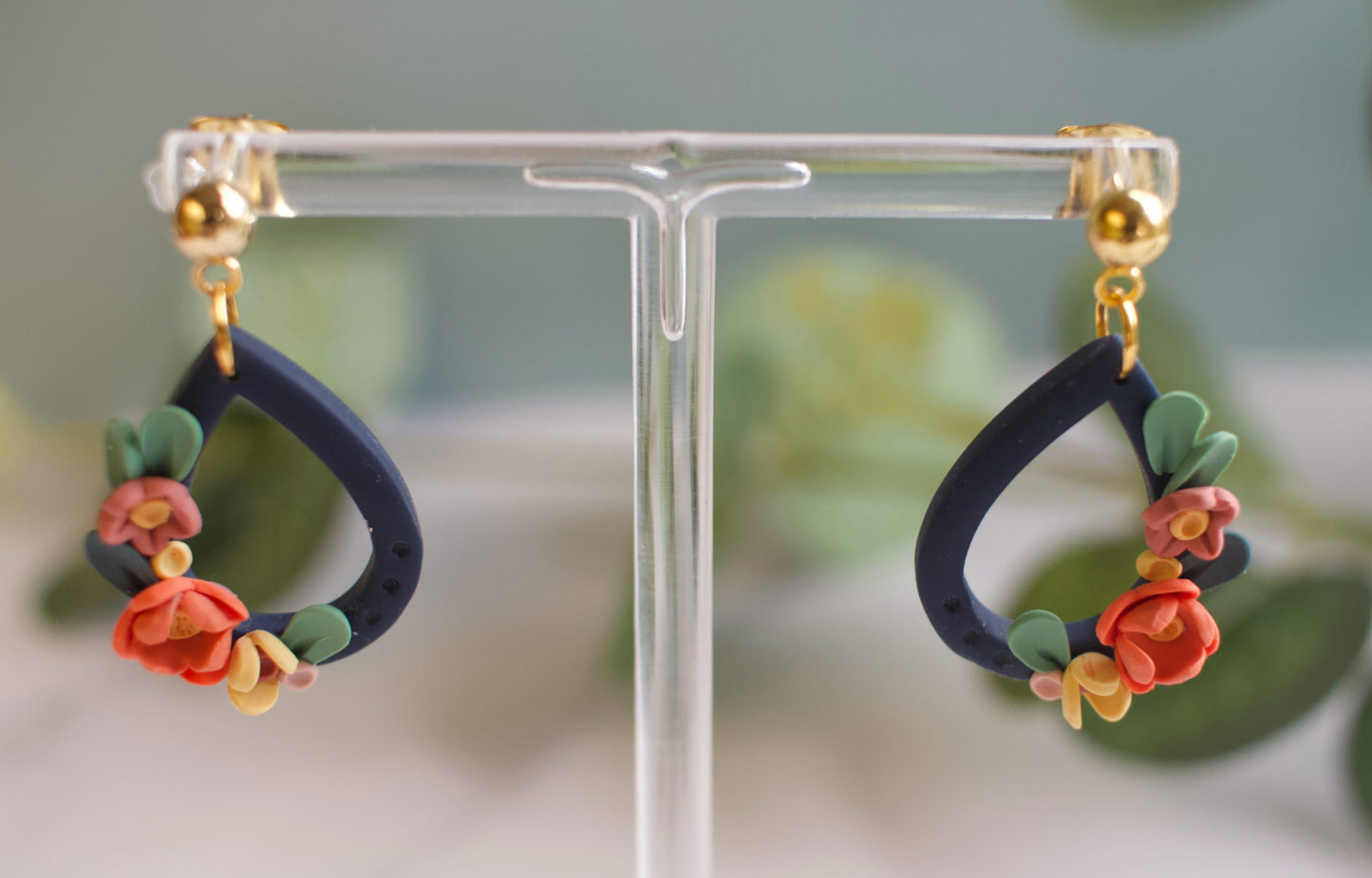 Pair of navy floral earrings on a clear stand with a blurred green background