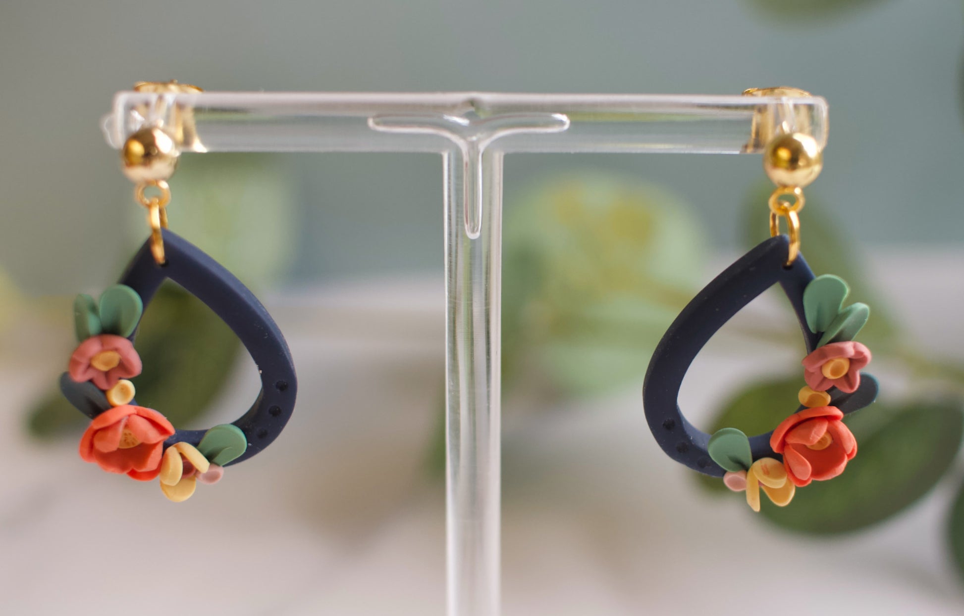 Pair of navy floral earrings on a clear stand with a blurred green background