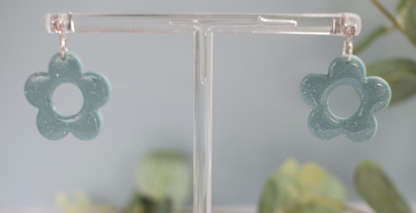 Flower-shaped earrings on a clear stand with a blurred green background