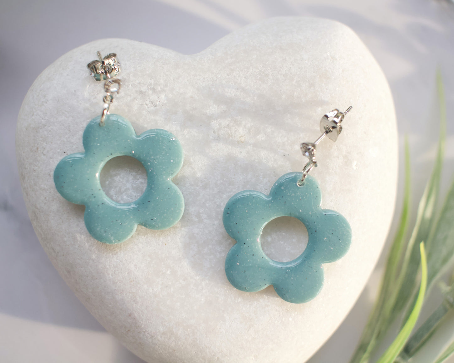 Pair of light blue flower-shaped earrings on a white heart-shaped stone.