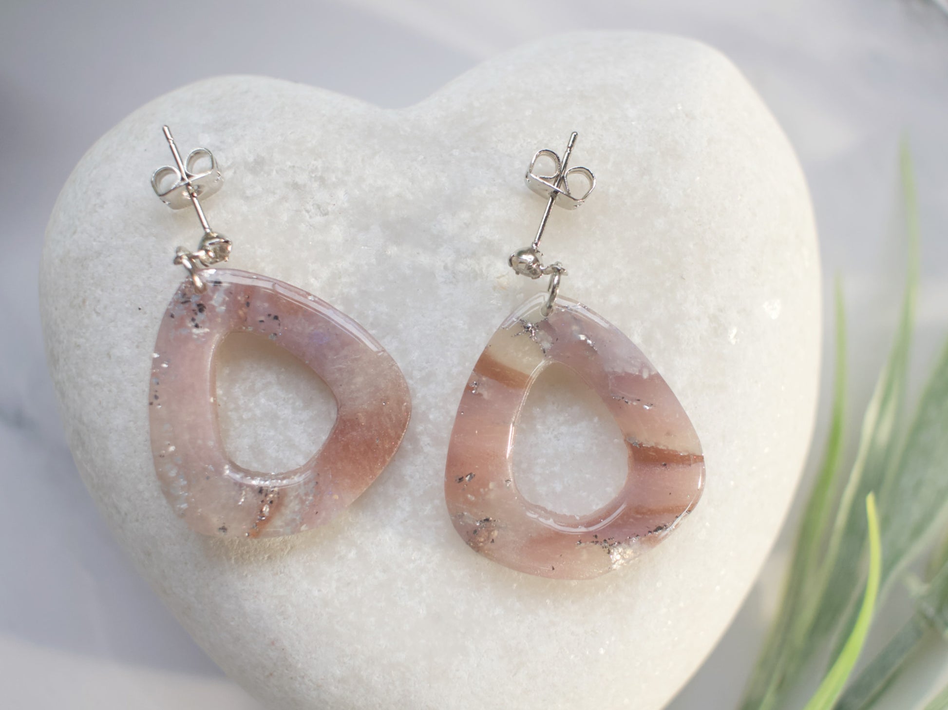 Pink and silver earrings on a white heart-shaped stone with grass in the background