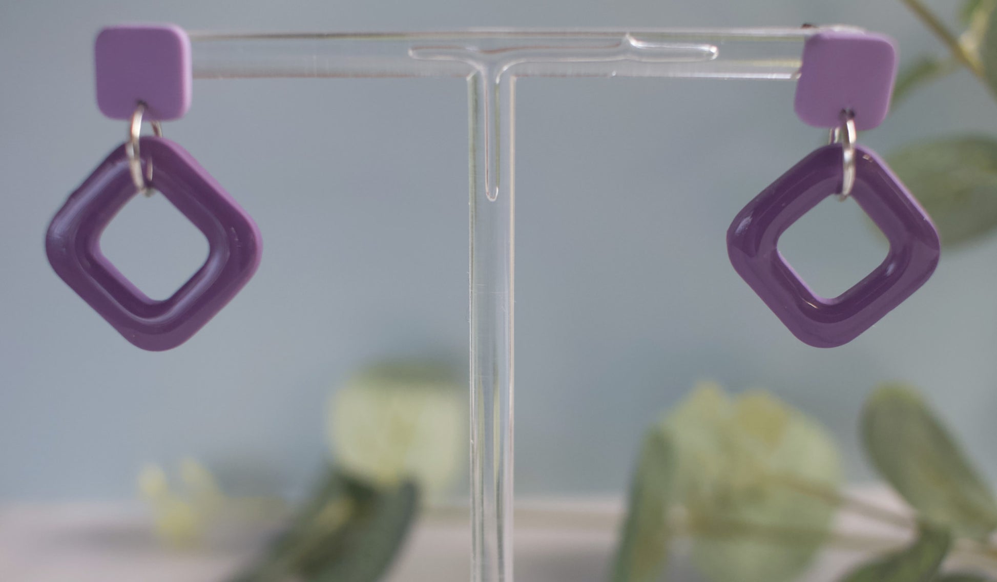 Purple square-shaped earrings on a clear stand with a blurred background