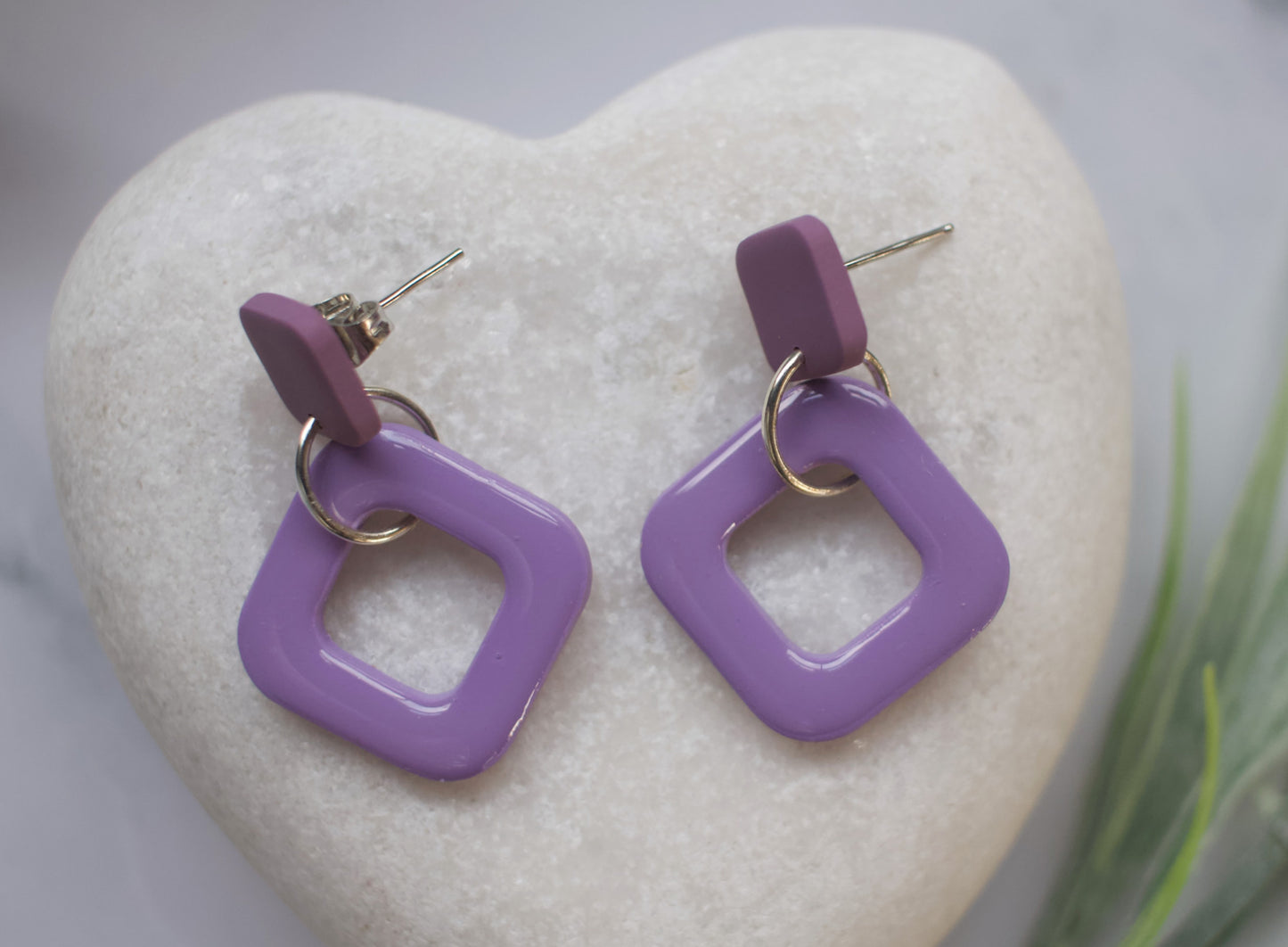 Purple square-shaped earrings on a heart-shaped stone with a blurred background