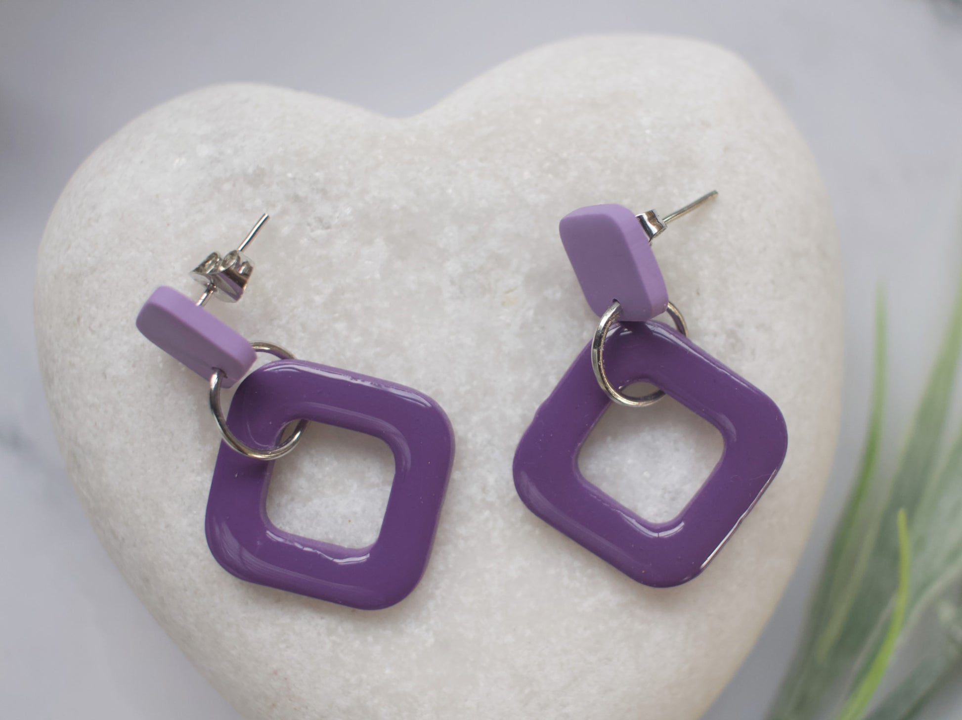Two tone purple off-set square earrings displayed on a white stone heart