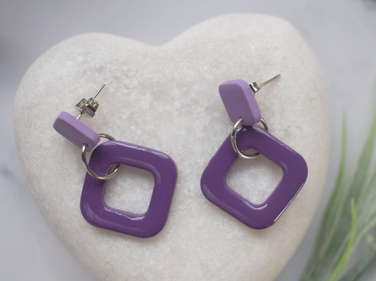 Two tone purple off-set square earrings displayed on a white stone heart