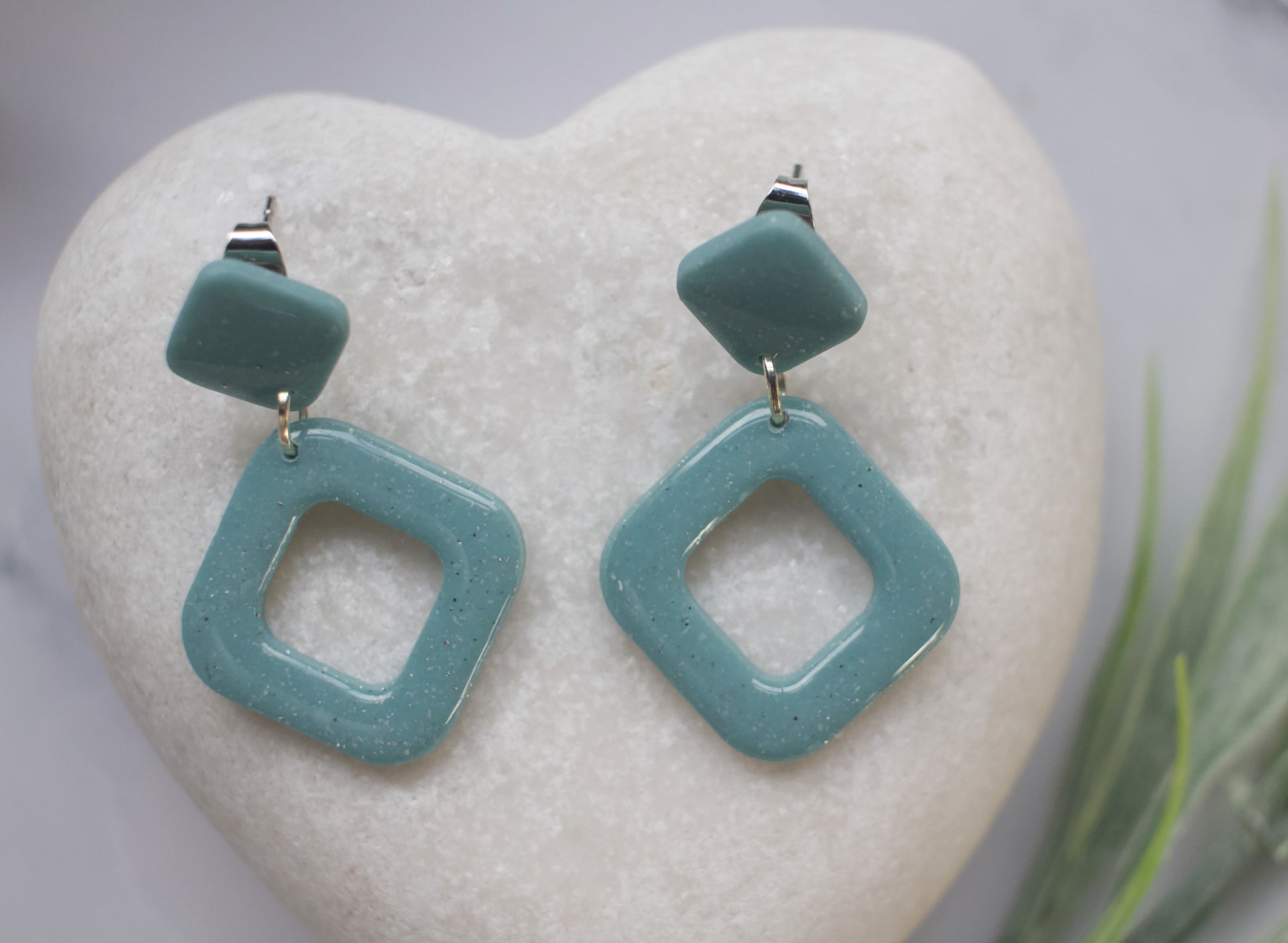 Teal square-shaped earrings on a heart-shaped stone with a blurred natural background