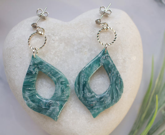 Green marbled earrings on a white stone with a blurred natural background